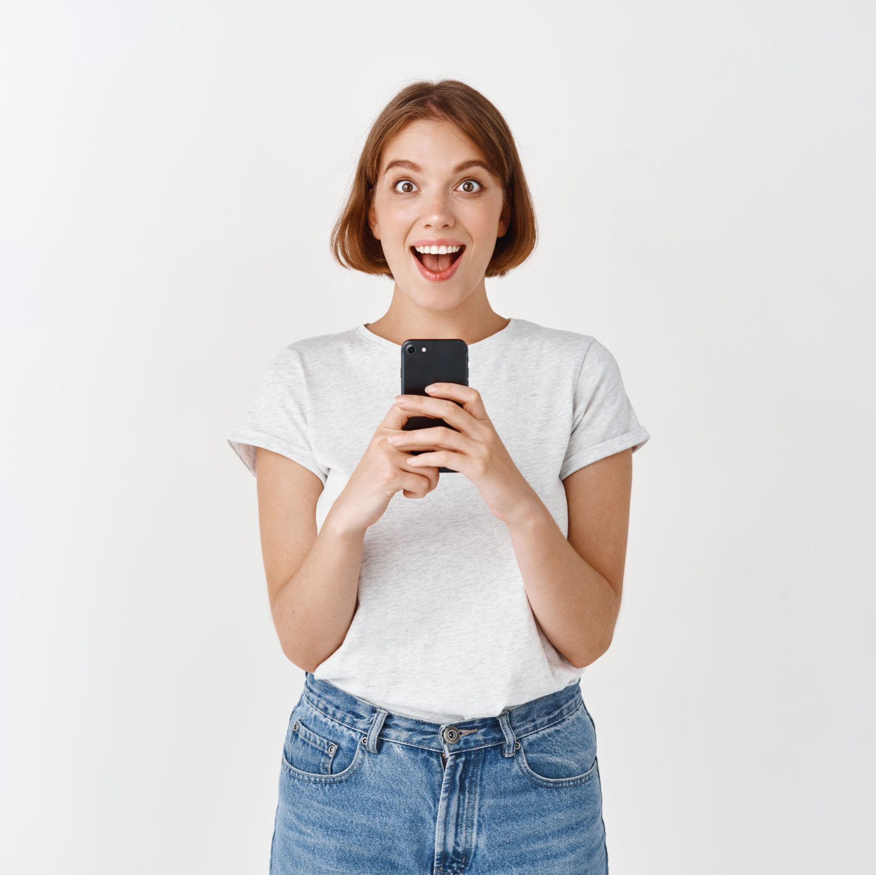 Excited pretty girl scream with joy after reading phone message, holding smartphone and looking amazed, checking out online promo, white background