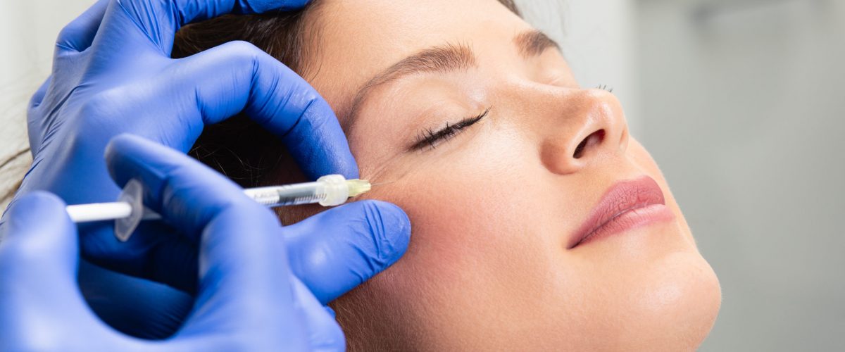 Attractive young woman is getting a rejuvenating facial injections. She is sitting calmly at clinic. The expert beautician is filling female wrinkles by hyaluronic acid. Attractive young woman is getting a rejuvenating facial injections. She is sitting calmly at clinic. The expert beautician is filling female wrinkles by hyaluronic acid.